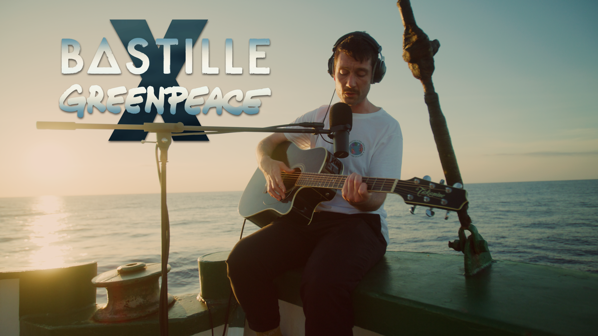 Dan from Bastille sitting on a boat with the sea and sunset behind him.